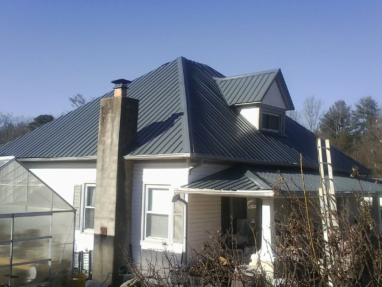 Dark blue standing seam metal roof on a white farmhouse with dormer — Slate & Tile Roof Repair by Roofing Brothers in West Kingston