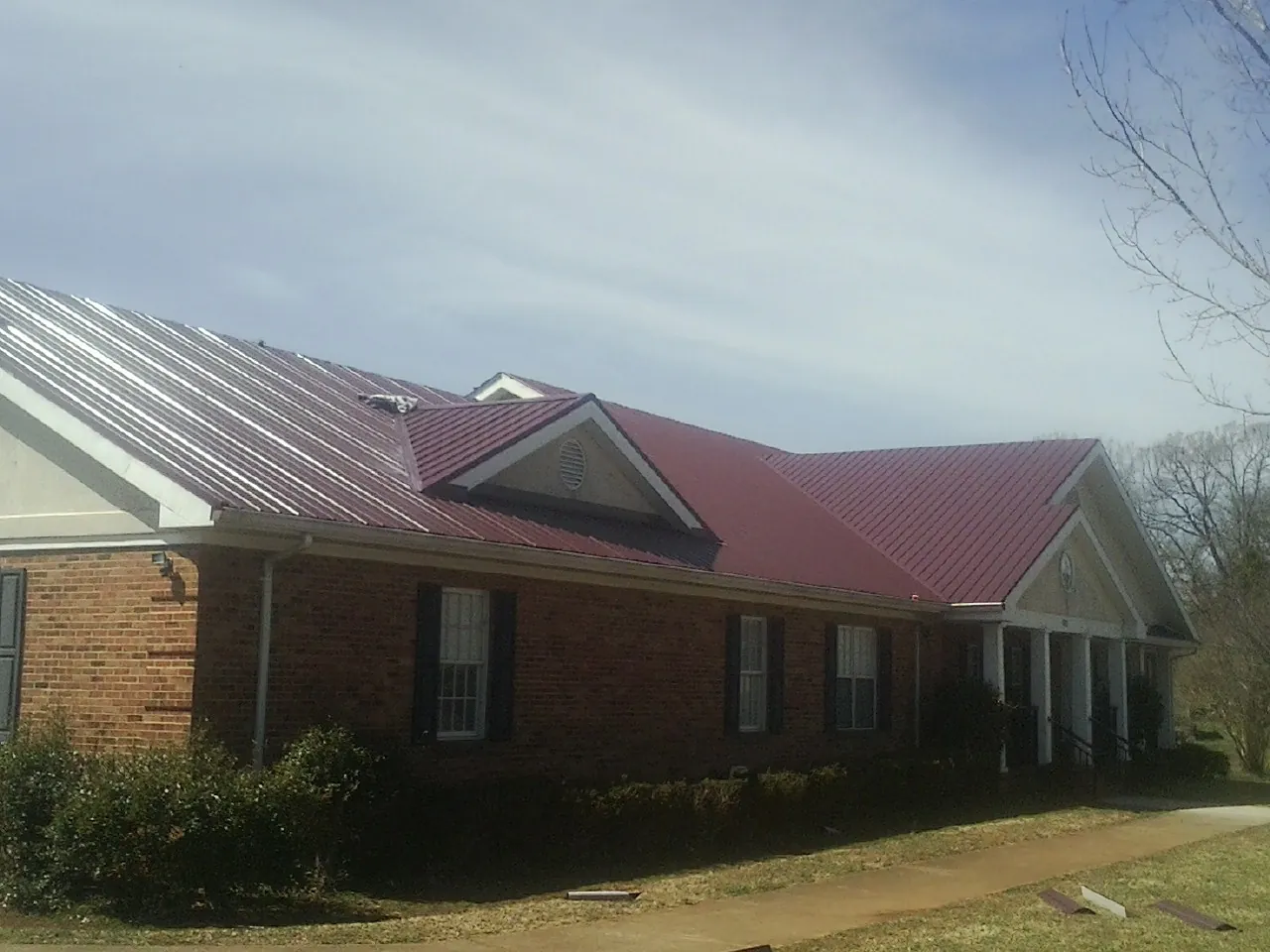 Red metal roof with gabled entries on a long brick building, from a Hail Damage Roof Repair job in West Kingston