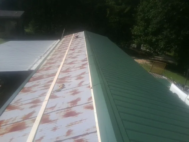 Old rusted panels beside newly installed green metal roofing — Wind Damage Roof Repair by Roofing Brothers in West Kingston