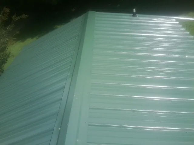New green metal panels meeting at the ridge of a roof — Flat Roof Repair work by our crew in West Kingston