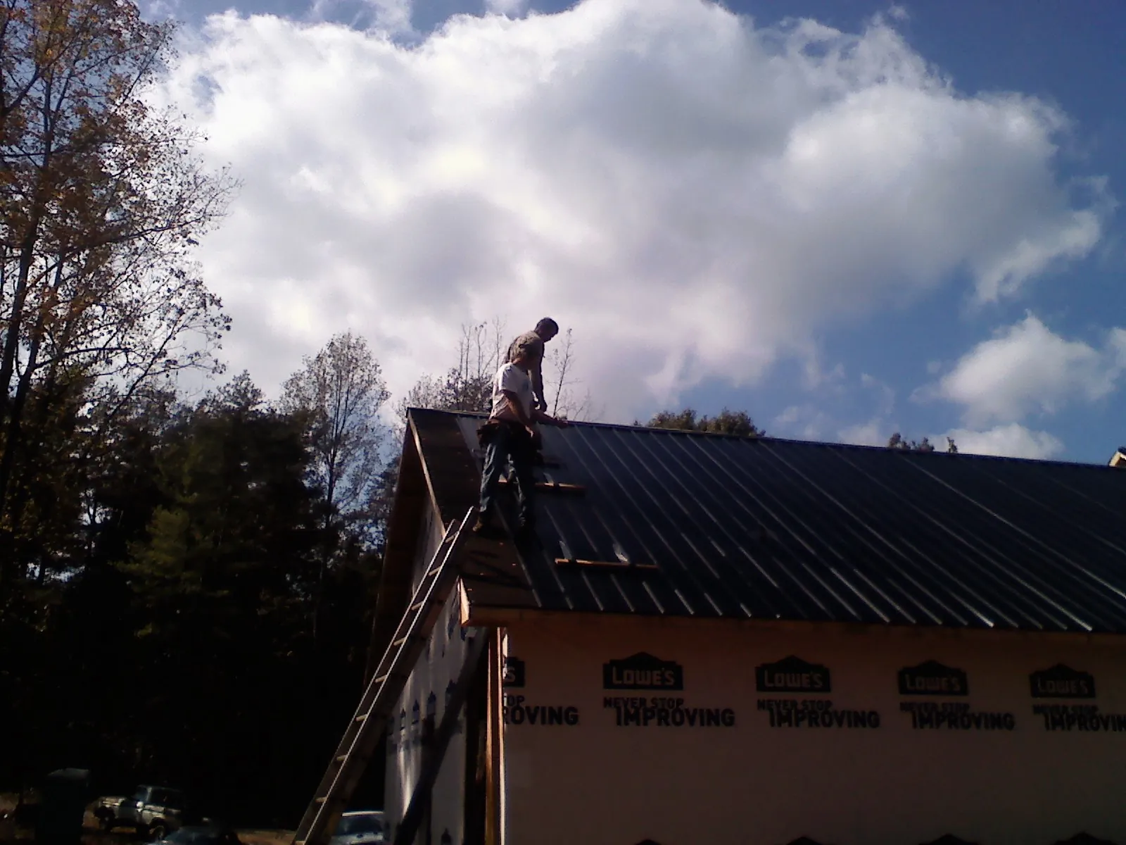 Roofer fastening dark metal panels high against a cloudy sky, from a Roof Inspection job in West Kingston