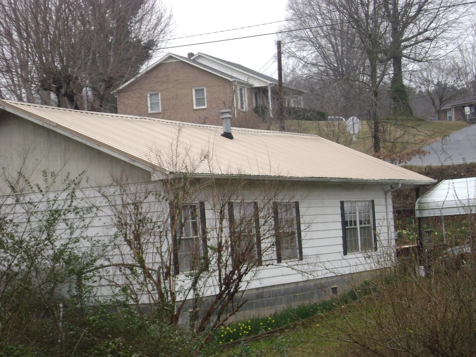 Tan metal roof on a white sided house set into a hillside — Commercial Roofing by Roofing Brothers in West Kingston