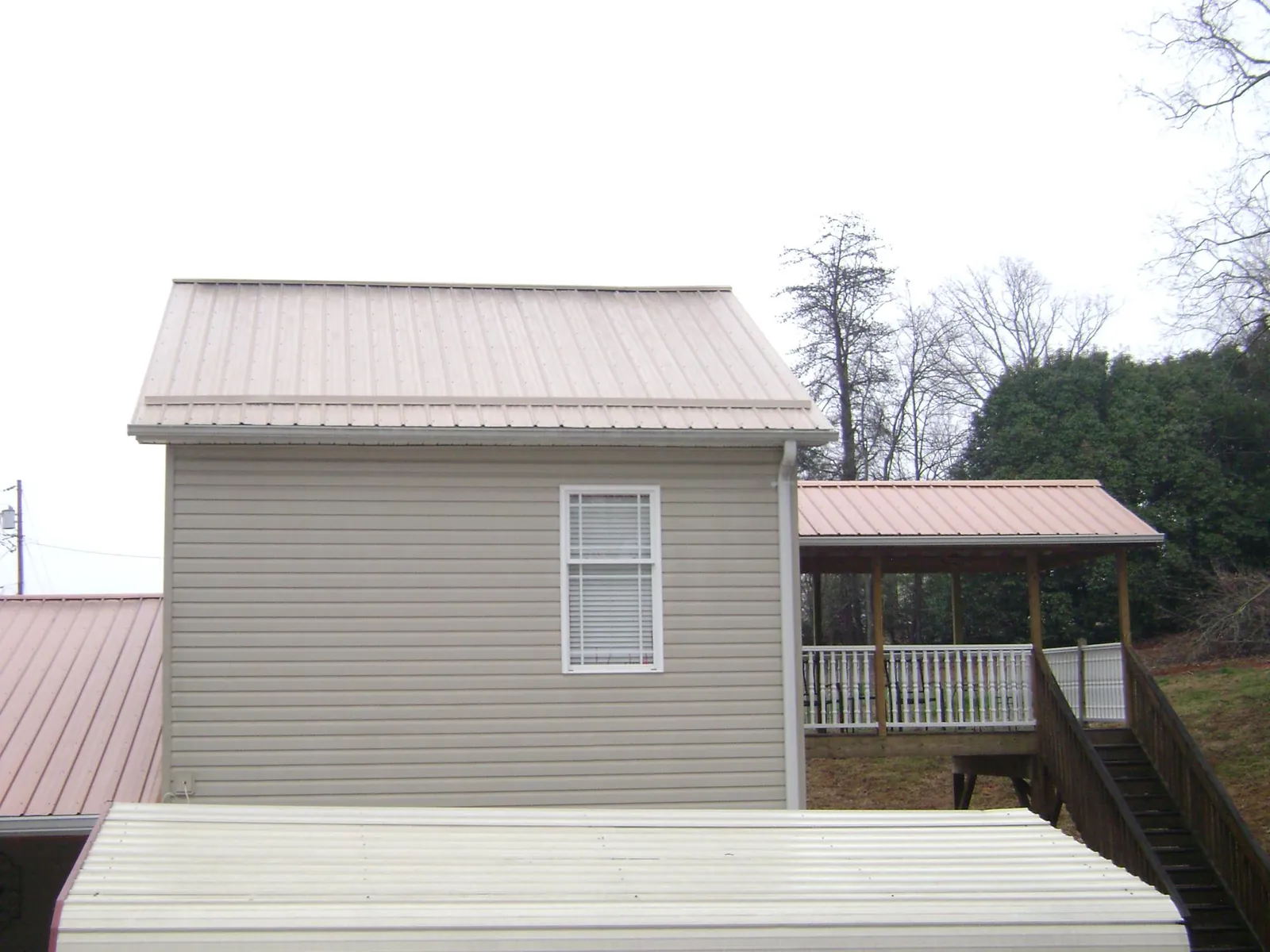 Tan metal roofs on a two story addition and attached porch, from a Roof Replacement job in West Kingston